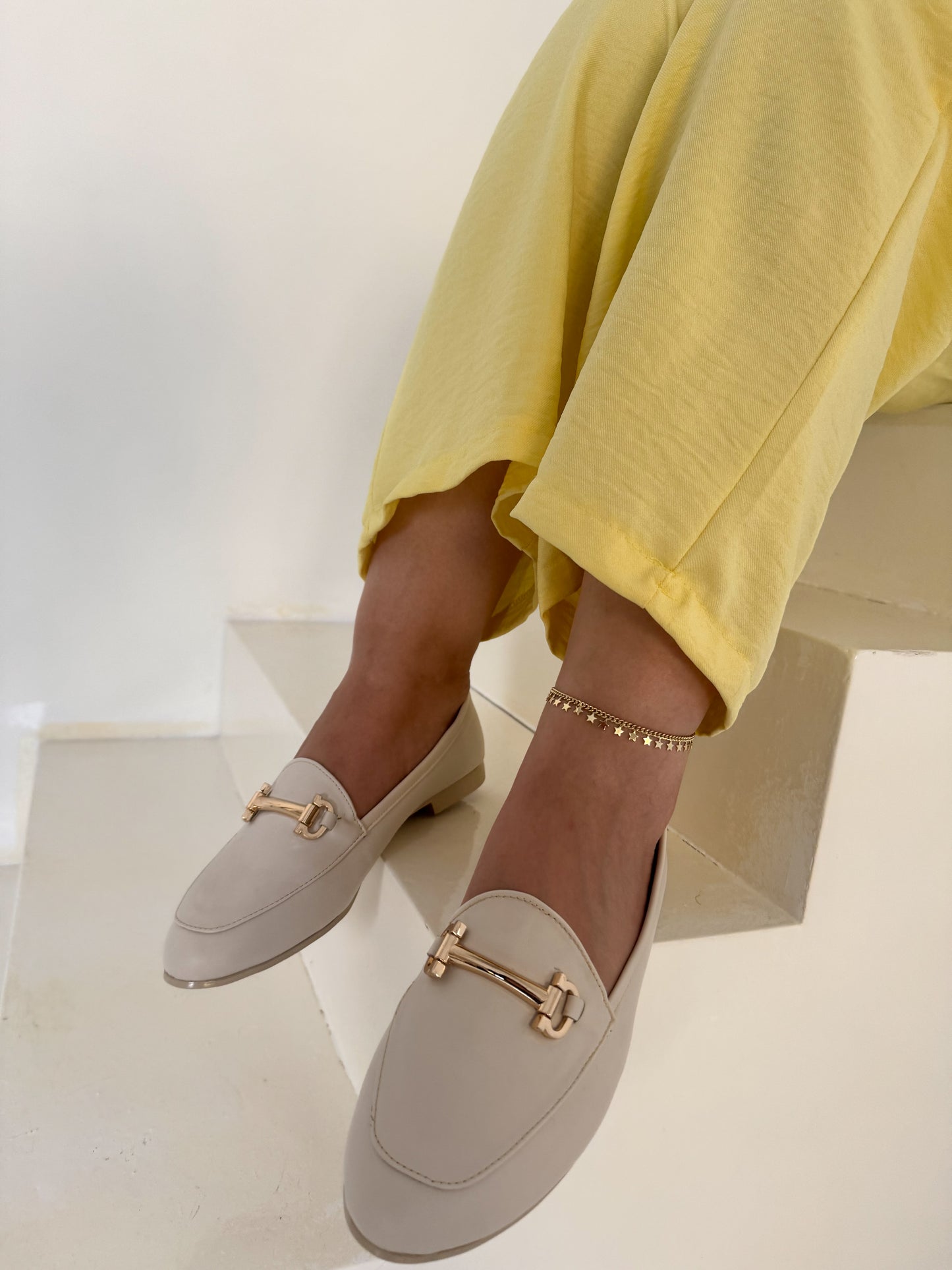woman wearing off white loafers with gold accents and yellow pants on a white background
