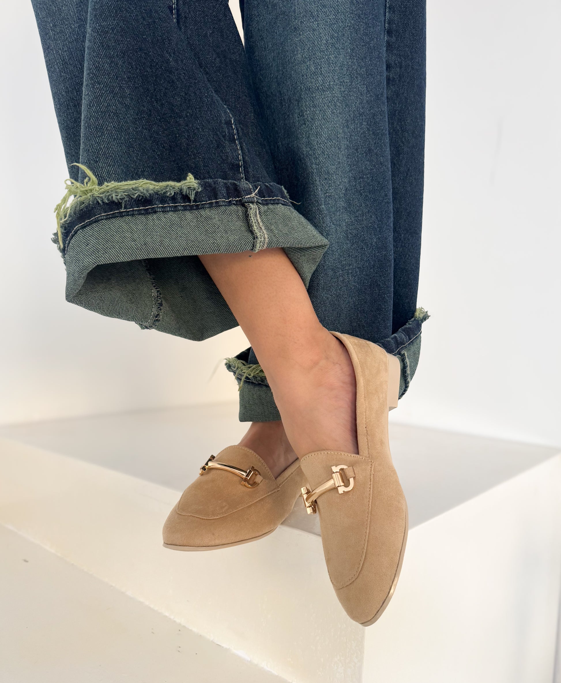 Beige loafers worn with rolled-up jeans on a white background