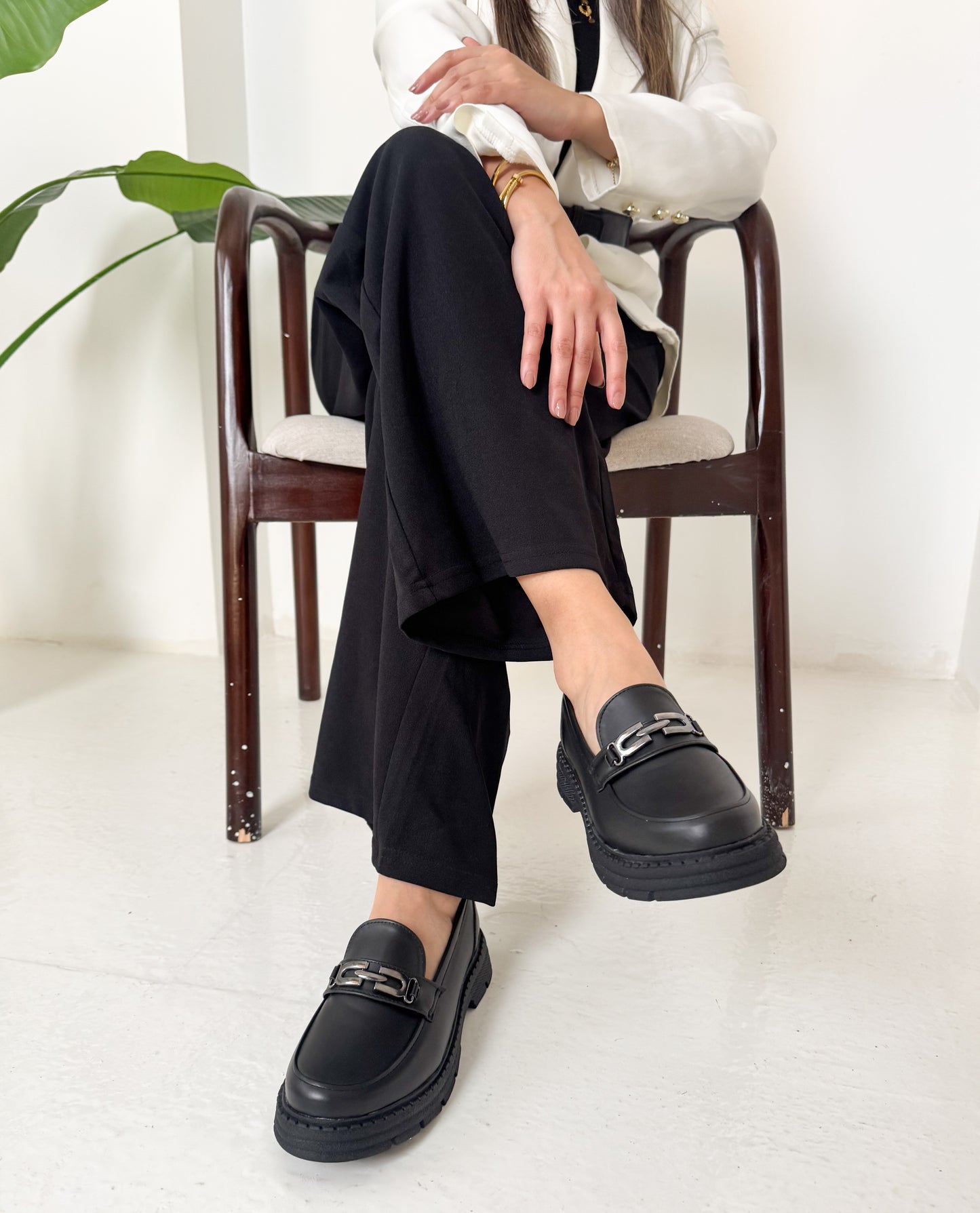 Woman wearing black loafers sitting on a chair with a white background